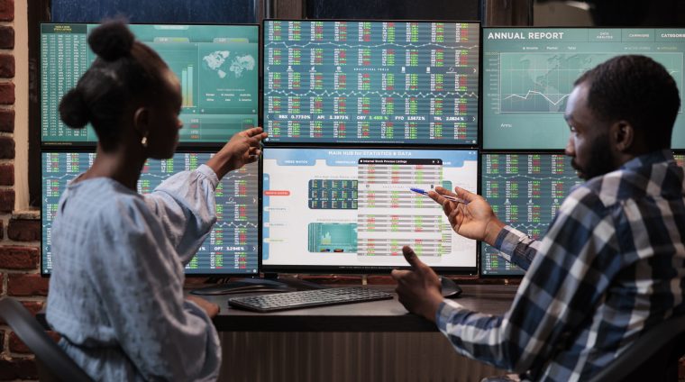 African american financial advisors reviewing real time market data and statistics in order to sell stocks. Hedge fund traders sitting at workstation while pointing at display with live index charts.