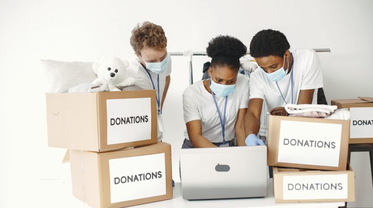 Guy and girl with check boxes. Volunteers in masks with laptop. Boxes with humanitarian aid.