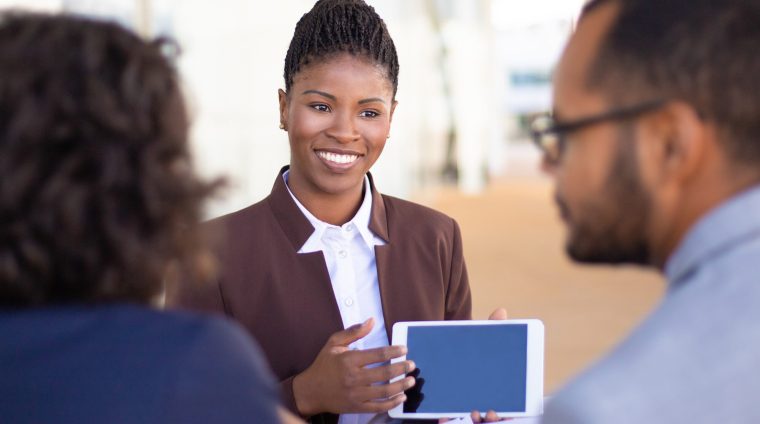 Joyful successful sales agent presenting content on tablet to clients. African American business woman speaking, smiling and showing blank tablet screen to colleagues or partners. Negotiation concept